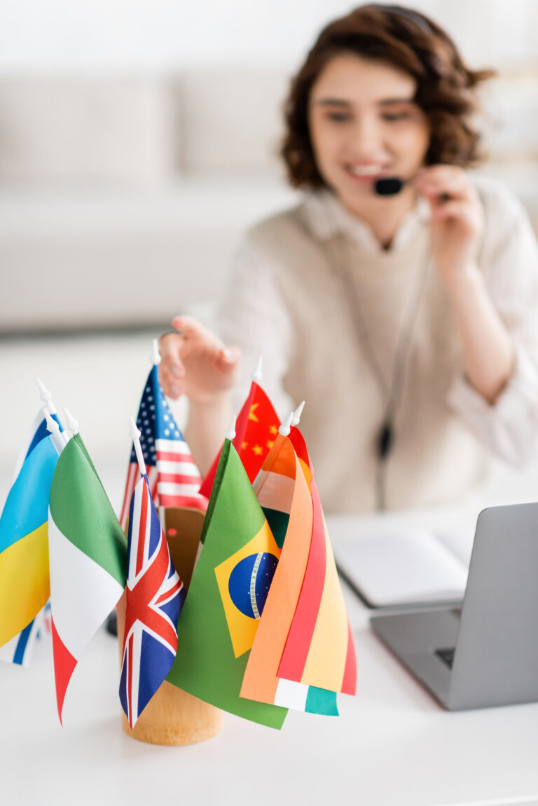 A person sat at a desk with a laptop, wearing a headset, in front of them is a pot full of various national flags